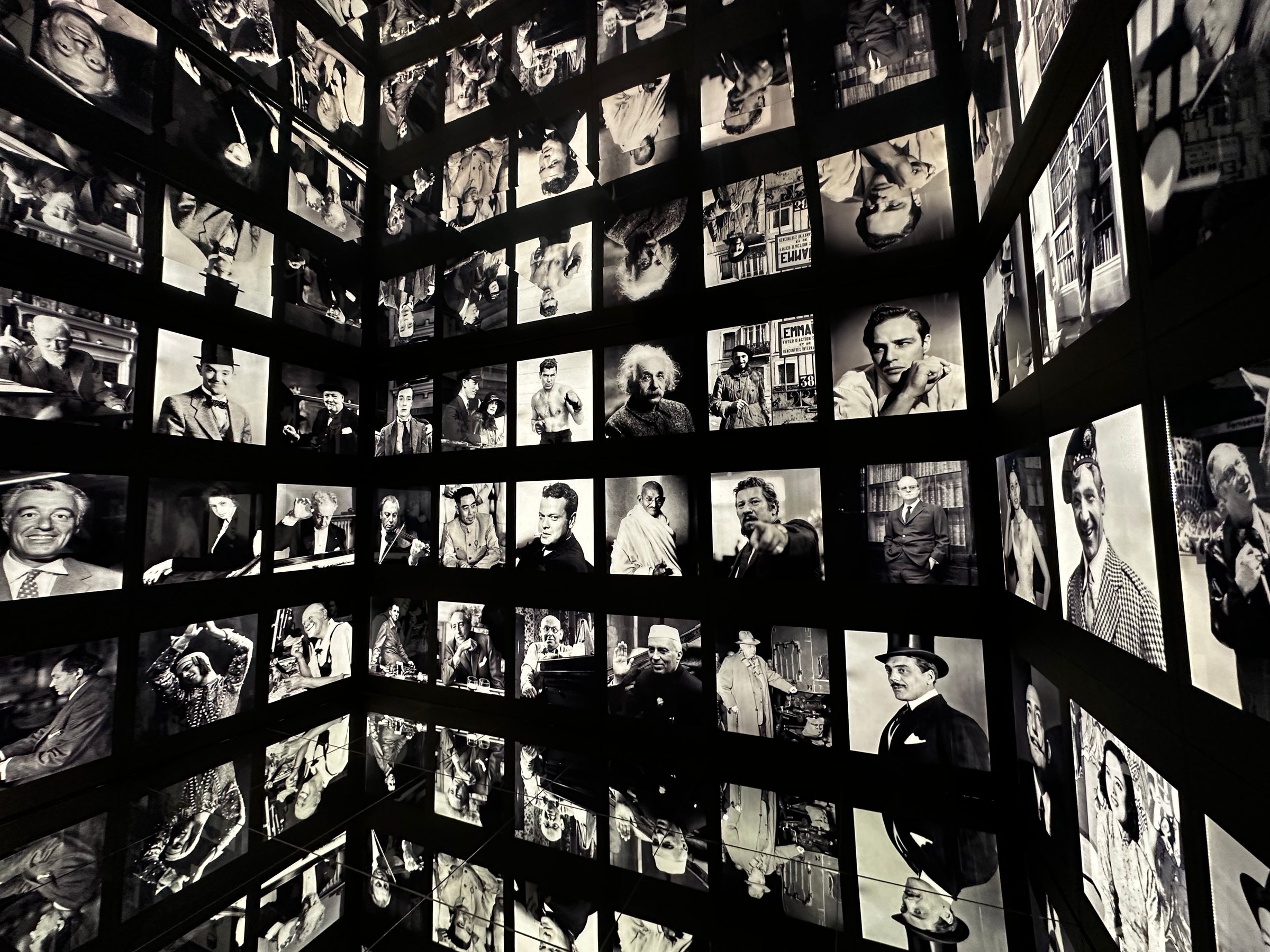 Mur de photos en noir et blanc, lumière tamisée, ambiance feutrée.