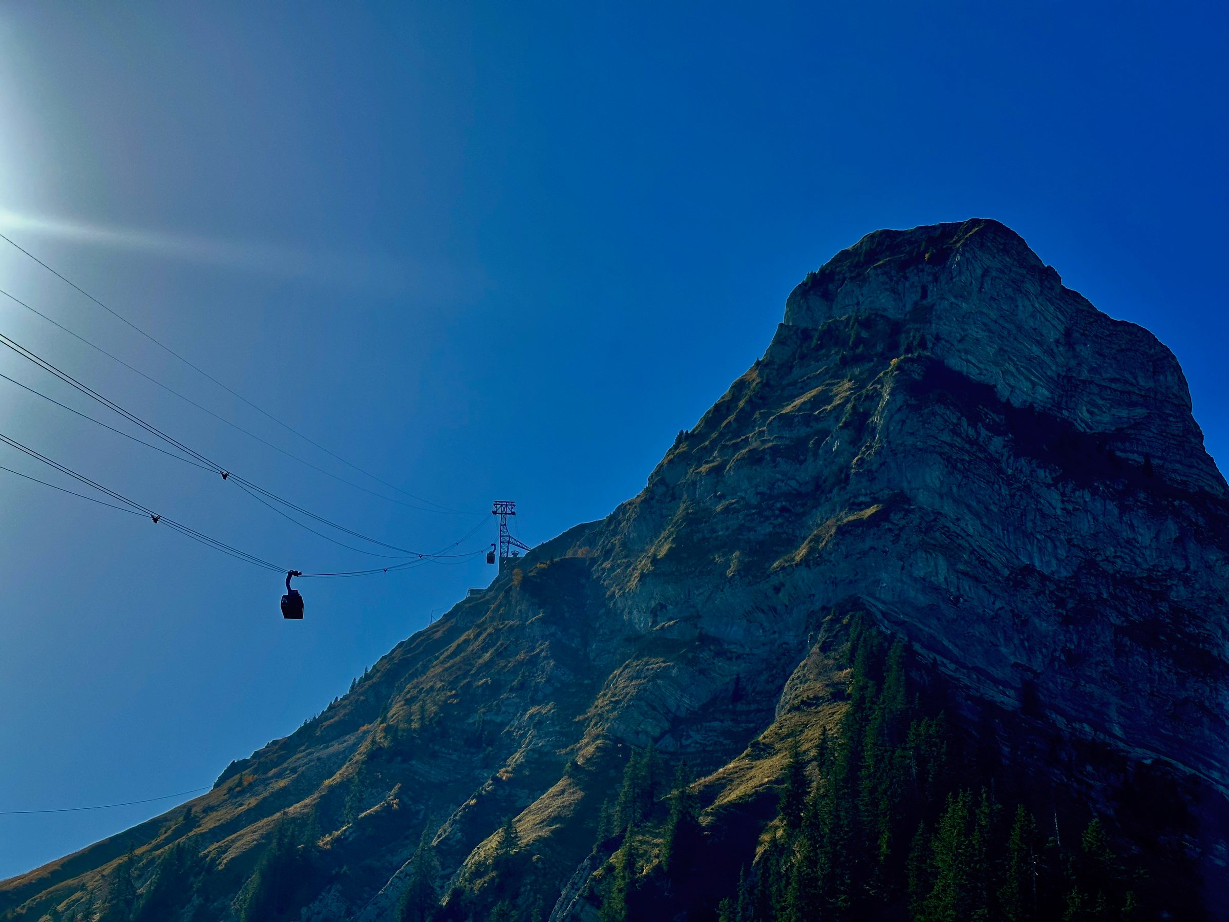Un câble de télécabine au pied d'une montagne escarpée sous un ciel clair. Lueur du soleil sur les rochers.